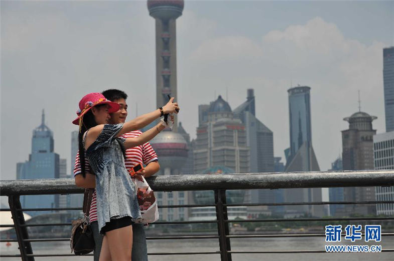 2013年6月17日，游客在上海外滩用手机自拍留影。当日，上海市气温快速上升，最高达到36℃。上海中心气象台10时33分发布2013年首个高温黄色预警信号。新华社发（刘晓晶摄）