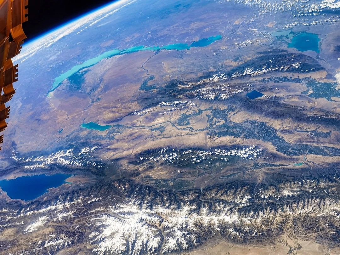 在太陽翼帆板與深邃宇宙所構成的夾角中，一條碧綠的玉帶溫柔地鋪在亞歐大陸上，這是“世界第四長湖”巴爾喀什湖，中國新疆的伊犁河自南而北注入巴爾喀什湖西部，使這條“中亞玉帶”呈現出西淡東咸的一湖兩水現象。照片左下角，深不見底的伊塞克湖如同一顆藍色的寶石深居在亞歐大陸的中心，一旁的雪山緊緊環繞，小心翼翼地將這美麗的湖泊從高原戈壁中輕輕托起。航天員劉伯明攝