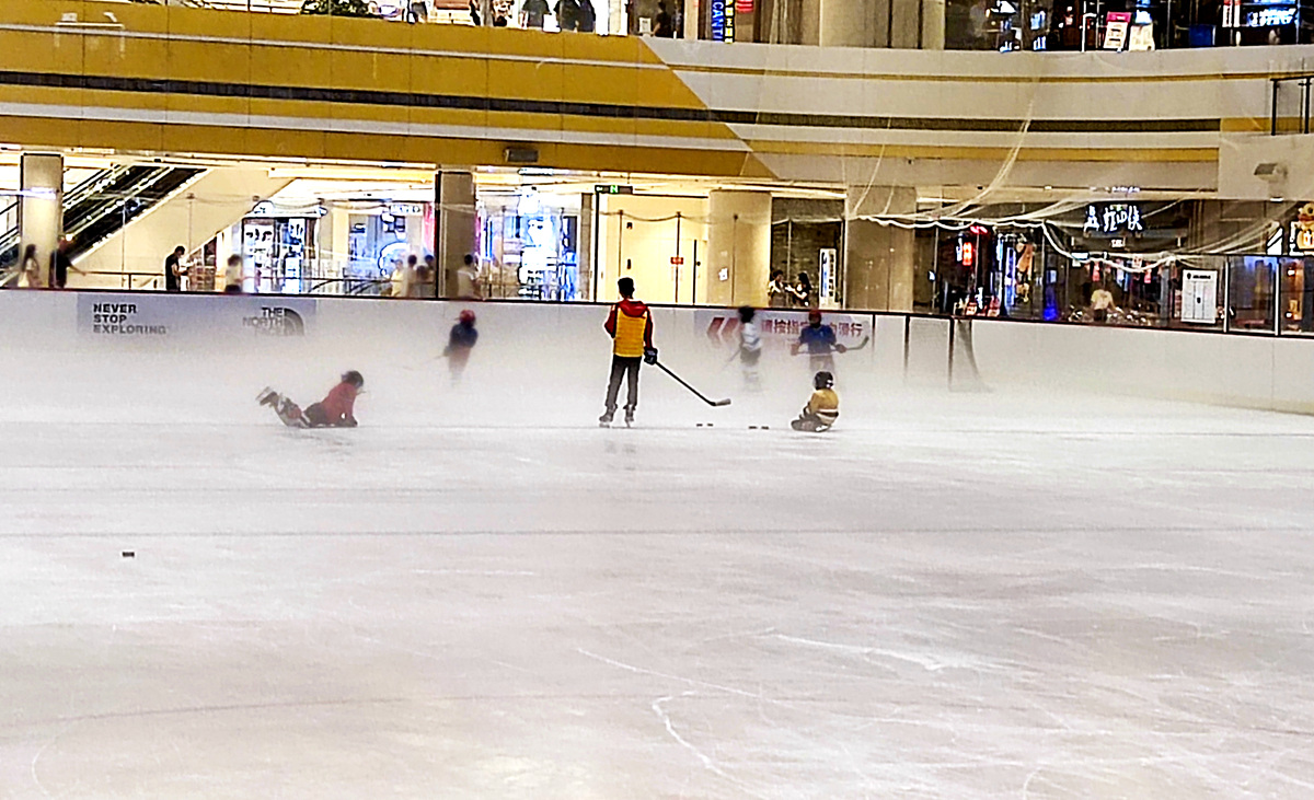 炎炎夏日，冰上运动是个不错的选择。图为晚上9点，夜间营业的商场内冰场上教练在带领孩子打冰球。人民网记者 孙博洋摄