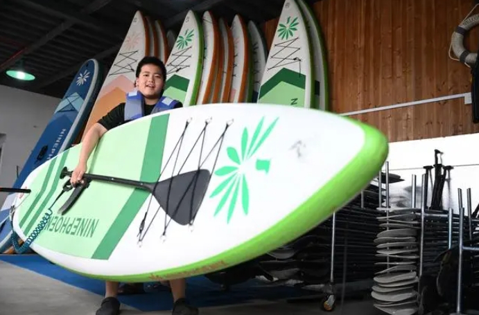 水上运动爱好者在搬运桨板	。为经济发展注入了新的活力。在刚刚过去的端午假期，全世界95%桨板器材产自中国。“清凉家电”掀起消费新“热浪”</p><p style=