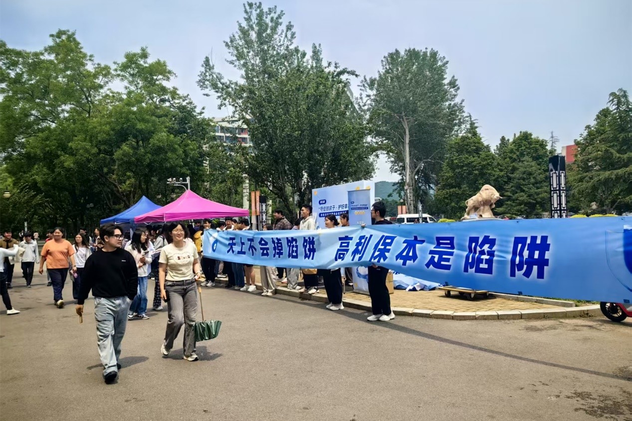 中國政法大學互動展台活動現場，學生們主動對 “天上不會掉餡餅 高利保本是陷阱”口號進行宣傳。