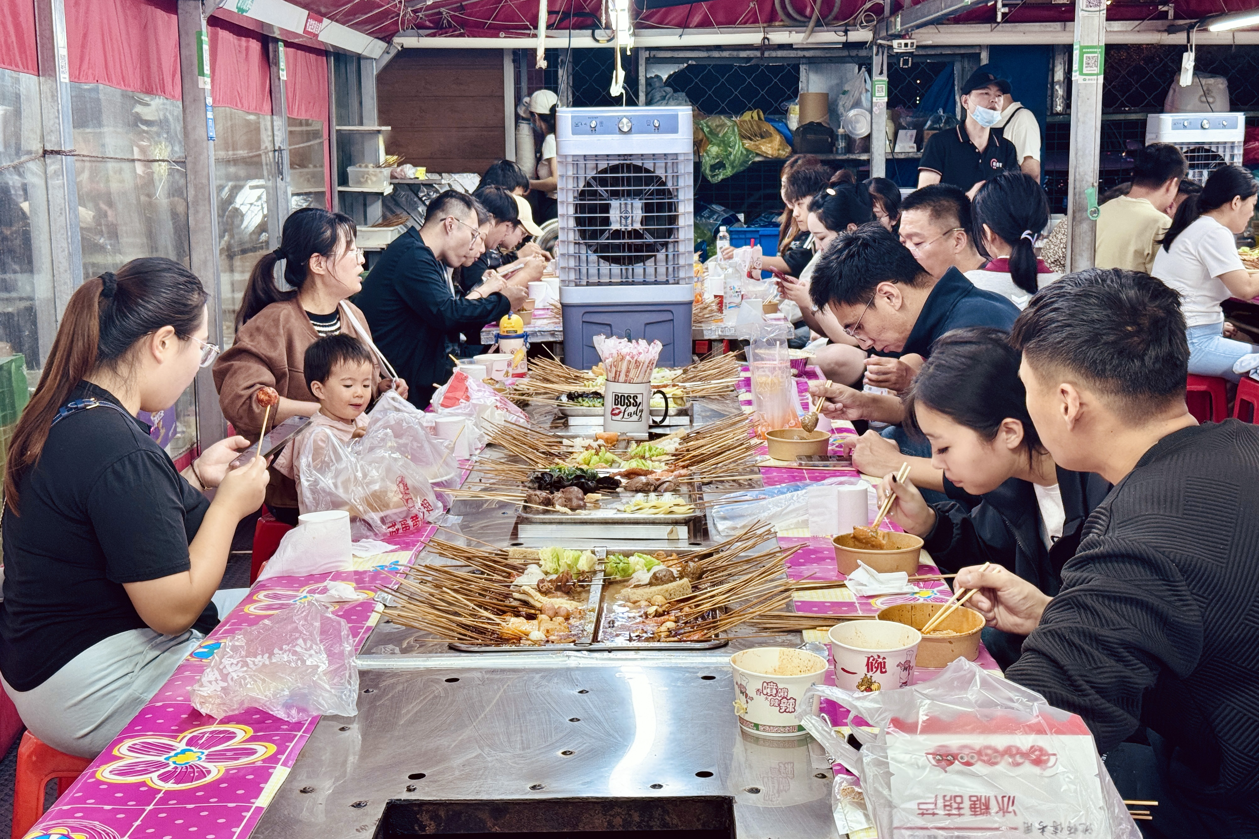 2025年9月28日，在山东省济南市环联夜市麻辣烫摊位旁，食客们围坐在烫锅两侧享受美食。人民网 郑昕桥摄