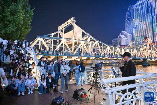 中外游客在天津海河岸邊聽青年歌手演唱（4月24日攝）。