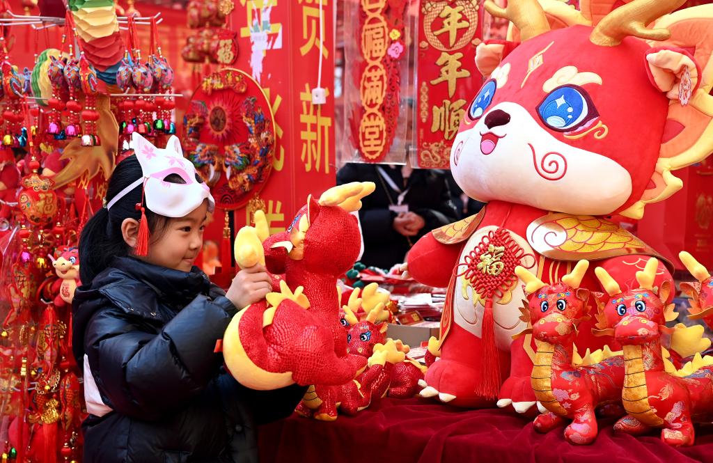一名儿童在西安一民俗年货节上玩赏生肖龙玩偶（1月30日摄）。新华社记者 刘潇 摄